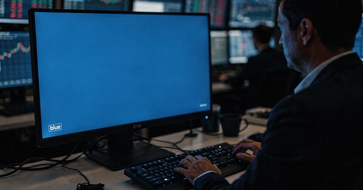 In an overnight dealing room lit only by screens, a trader cropped at the chin types as a monitor fills with a solid color field labeled "blue".