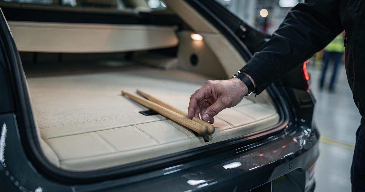 Close detail in cool early-morning light at a car factory end-of-line inspection bay, a worker's hand cropped at the knuckles setting a pair of wooden.