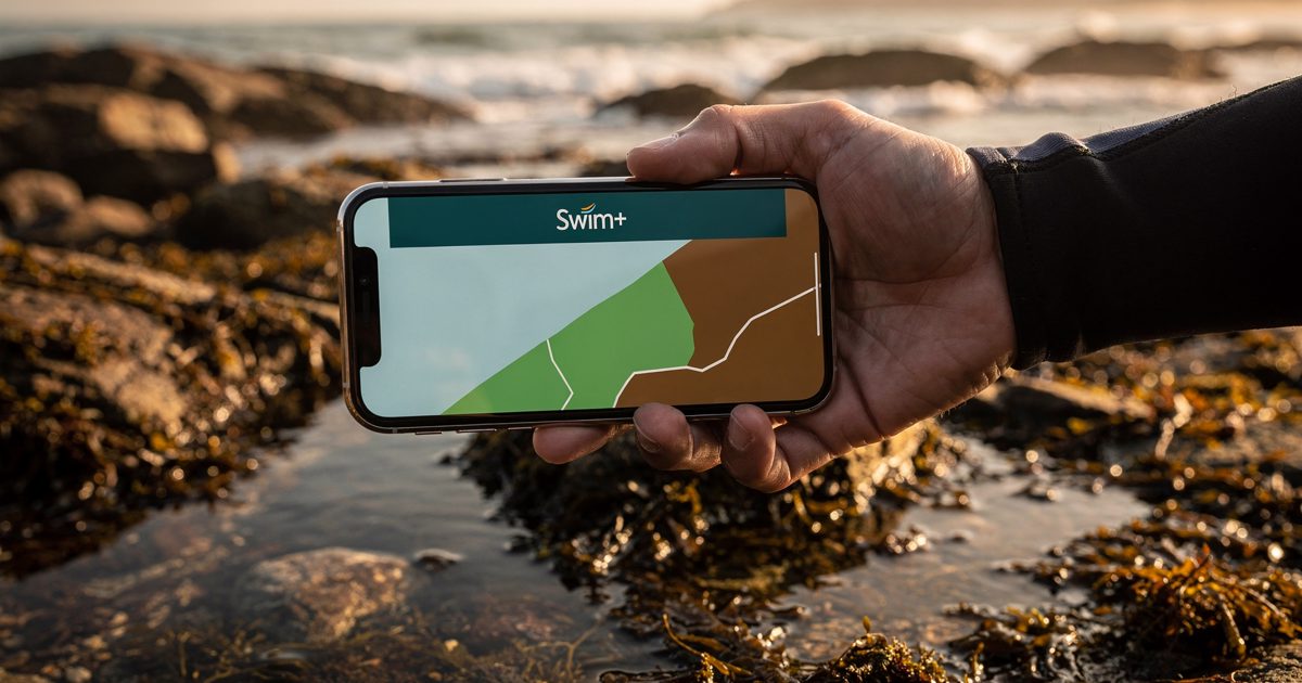 Close shot at golden evening light of a hand holding a phone above a shoreline rock pool, the screen showing a coastal map split into green and brown zones.