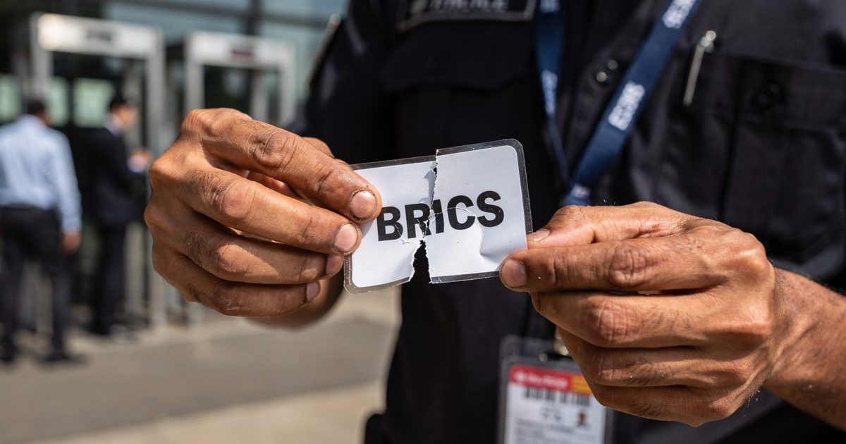 Close detail in harsh afternoon sunlight outside a New Delhi conference centre, a security guard's bare hands tearing a temporary credential badge reading.