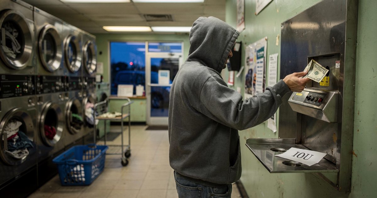 Eye-level medium shot inside a strip-mall laundromat under flat fluorescent light at dusk, a customer seen from behind in a hooded sweatshirt feeding a dollar.