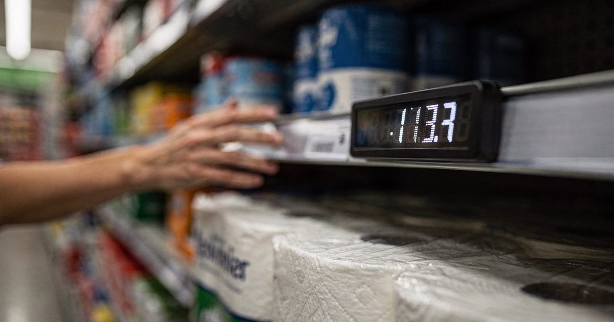 Extreme close shot in a big-box store aisle under flat fluorescent light of a small electronic shelf-edge price display mid-refresh, its digits caught.