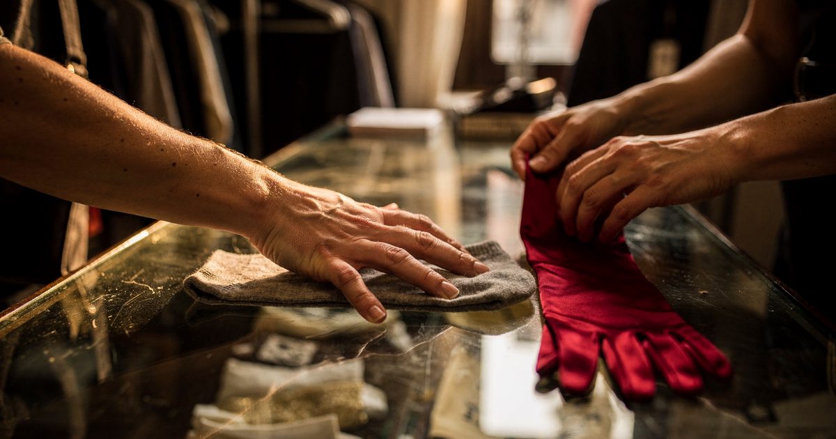 Close detail in warm late-afternoon light inside a narrow Brooklyn clothing boutique, a customer's forearm cropped by the frame pressing a grey sock to a glass.