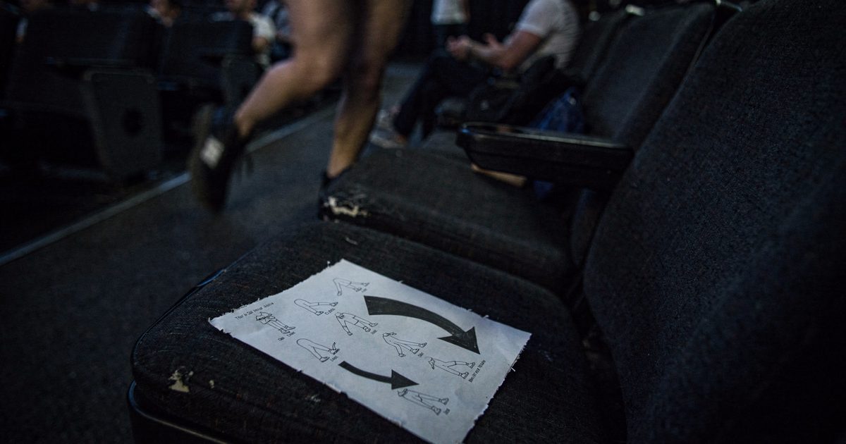 Close pre-dawn shot inside a cinema auditorium of a stapled dance instruction sheet resting on a fold-down seat, its last arrow curving back to the first line.