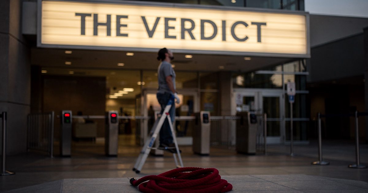 Dusk neon glow outside a Las Vegas courthouse entrance as a worker on a stepladder, face tilted up and out of focus, slots plastic letters spelling "THE.