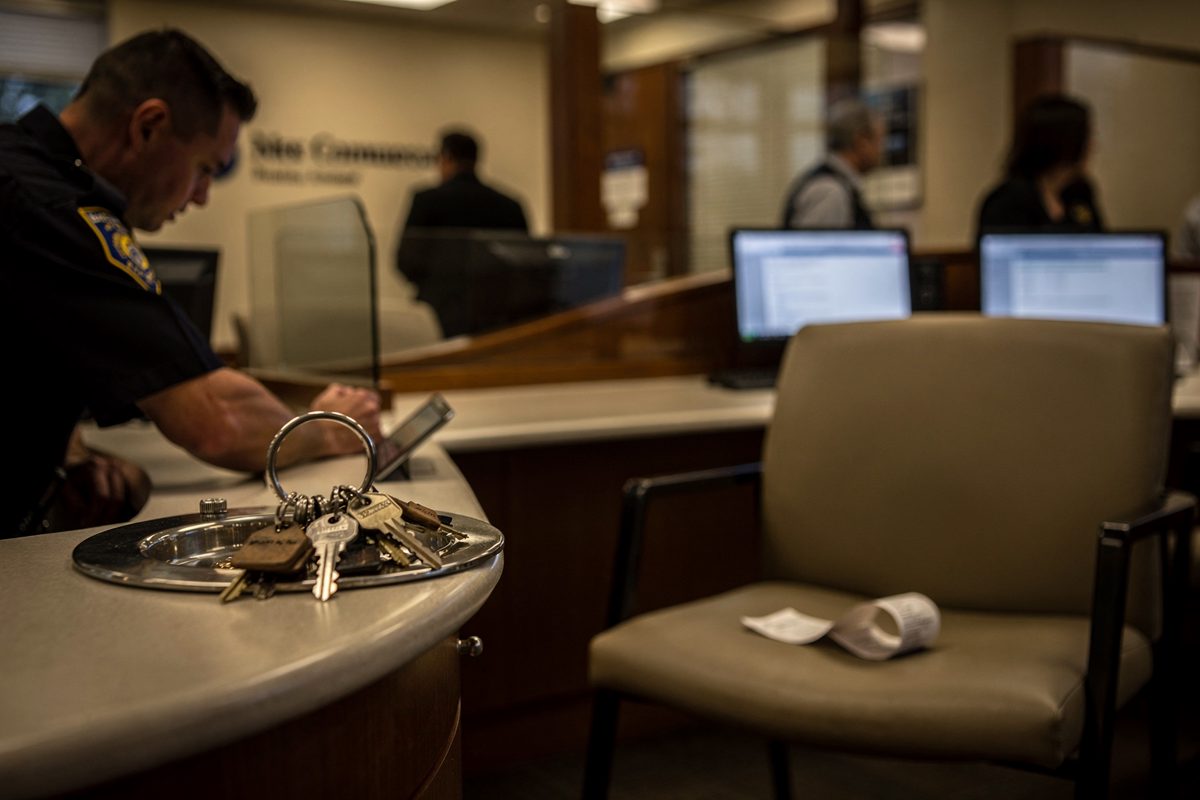 Under warm evening lamps in a bank lobby just after closing, a guard in soft profile rests a ring of keys on a coin tray while a curled receipt sits on the.