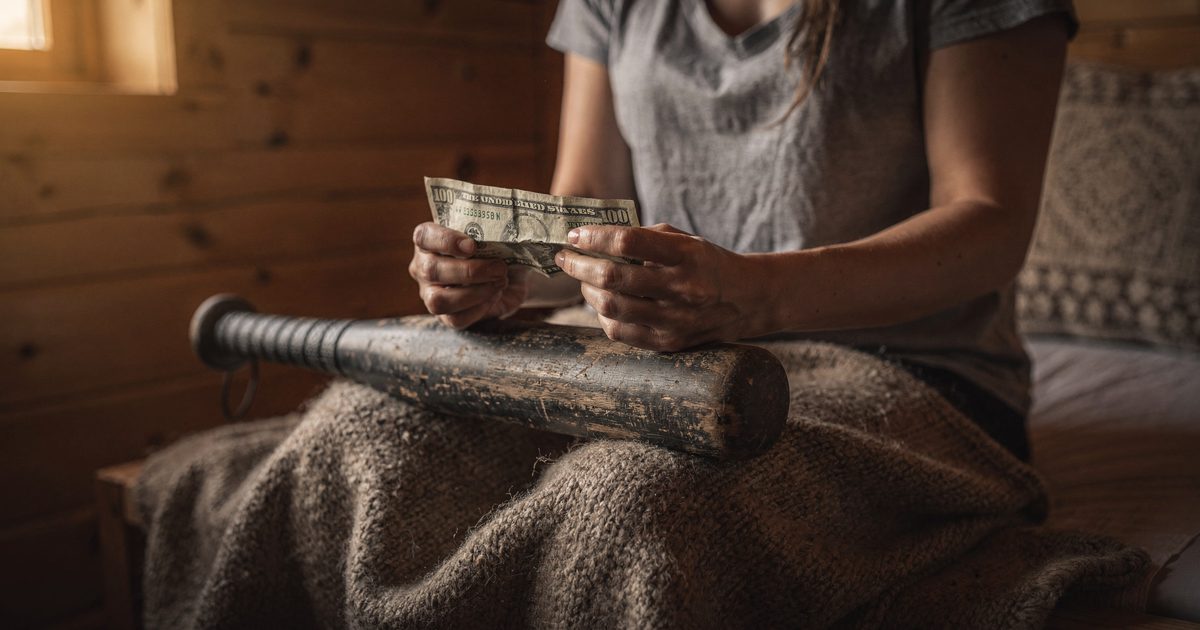 Close detail in a pine-walled retreat cabin at early morning with low sun through a side window, a woman's hands seen from the wrists down gripping a folded.