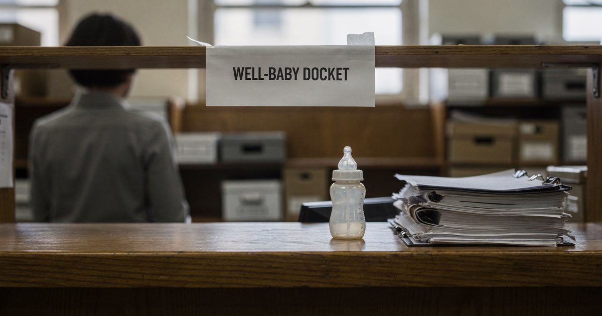 Medium shot in pale morning light inside the Supreme Court public filing room, a clerk seen from behind at a wooden counter beneath a paper sign reading.