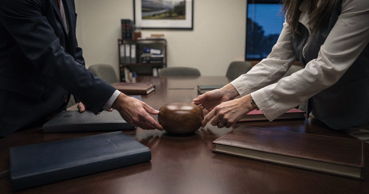 High-angle shot in cool blue hour light inside a ground-floor side office of the U.S. Capitol, two staffers cropped at the shoulders as they set a smooth round.