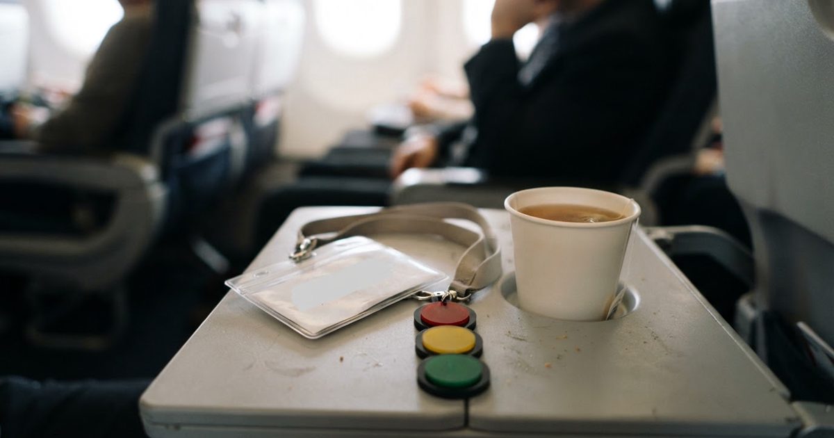 A close-up of a conference name tag lanyard with a color-coded traffic light system attached, resting on an airplane tray table next to a cup of herbal tea.