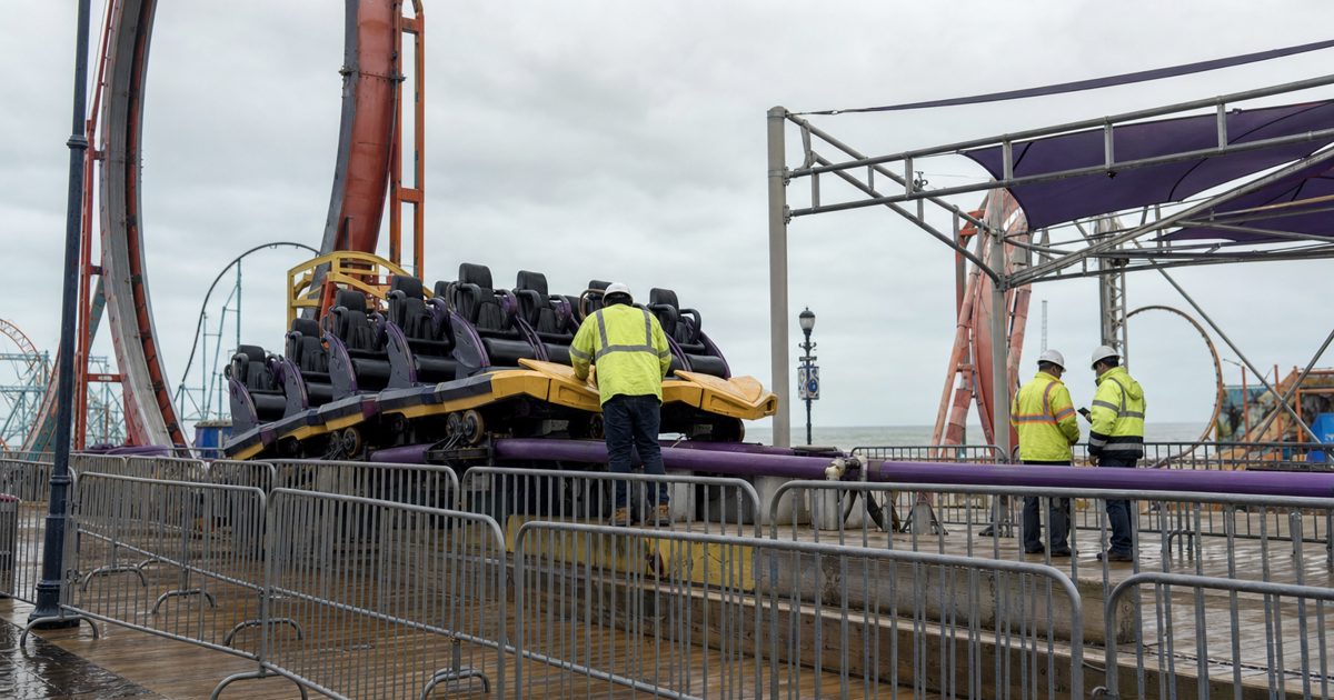 Documentary news photograph of an empty seaside amusement park ride paused during an inspection, safety barriers around the platform, engineers in reflective.
