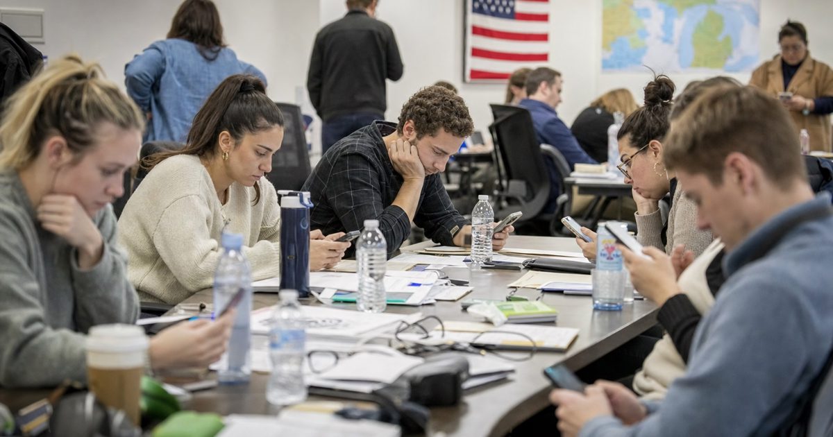Documentary news photograph inside a Michigan campaign office, anonymous staff members gathered around a conference table checking vibrating smartphones, tense.