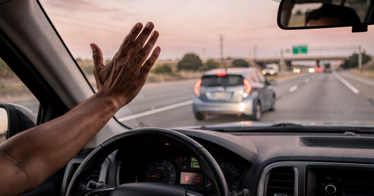 Dashboard-level shot from inside a pickup truck cab in pink sunrise light on an Austin interstate, the driver visible only as a forearm out the open window.