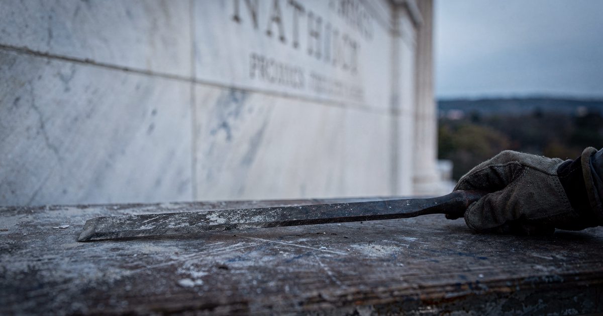 Close detail in cool early-morning light of a stonemason's flat chisel resting untouched on a scaffold plank against pale marble cladding, a gloved hand.