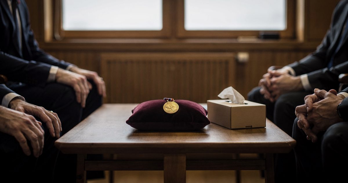 Close detail inside a small wood-panelled meeting room in Oslo in pale northern morning light from a tall window, a gold medal resting on a velvet cushion on a.