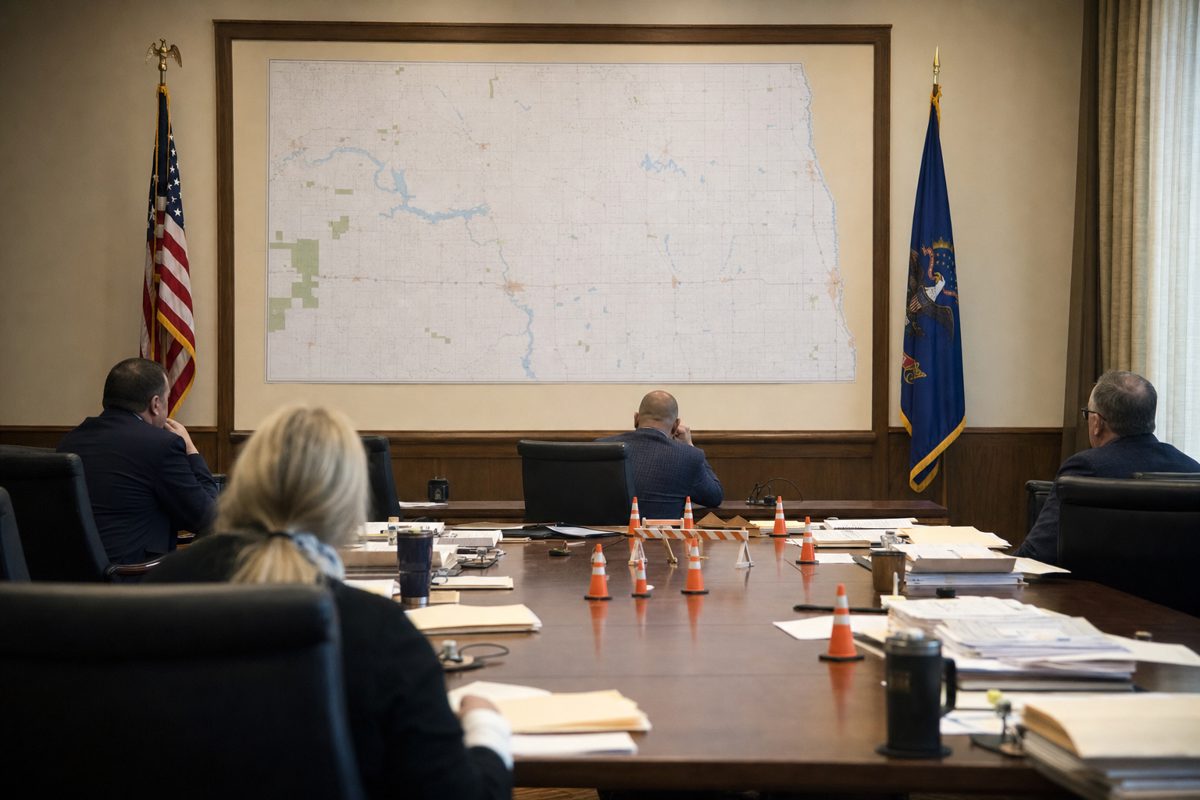 A realistic government conference room in North Dakota with a large blank wall map, folders, laminated badges and miniature traffic barriers arranged on a long.