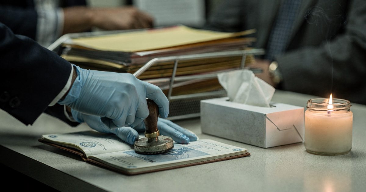 Close-up under harsh fluorescent light in a federal processing office of gloved hands pressing a rubber stamp onto an open passport, a box of tissues and a.