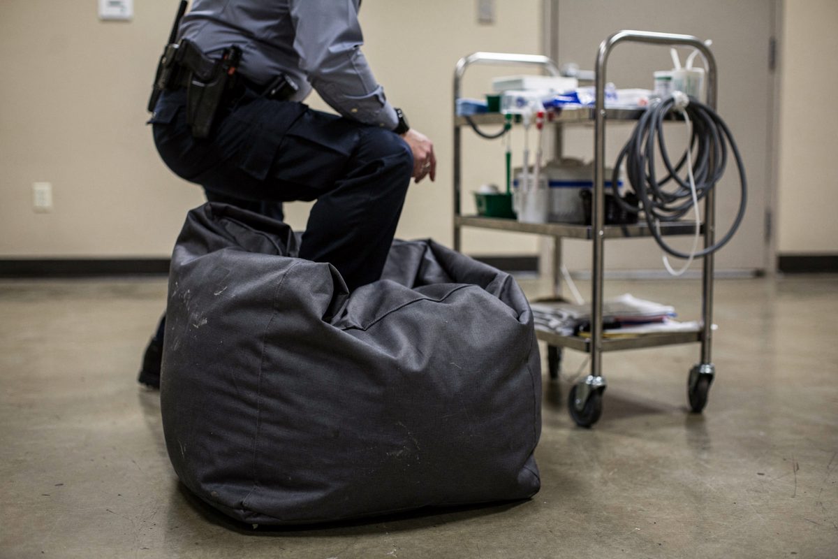 Eye-level detail under flat fluorescent light in a bare corrections training room, a single beanbag chair placed on a polished concrete floor directly in front.