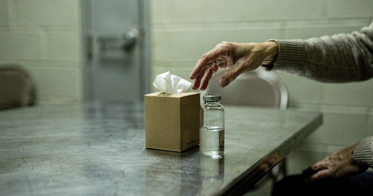 Close detail on a steel table in a Tennessee prison visiting room under cold fluorescent light, a cardboard box of tissues standing next to a single clear.