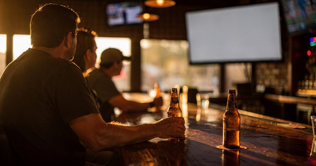 Golden late-evening sunlight slanting through the front window of a Houston sports bar, three patrons framed from the shoulders down on barstools all turned.