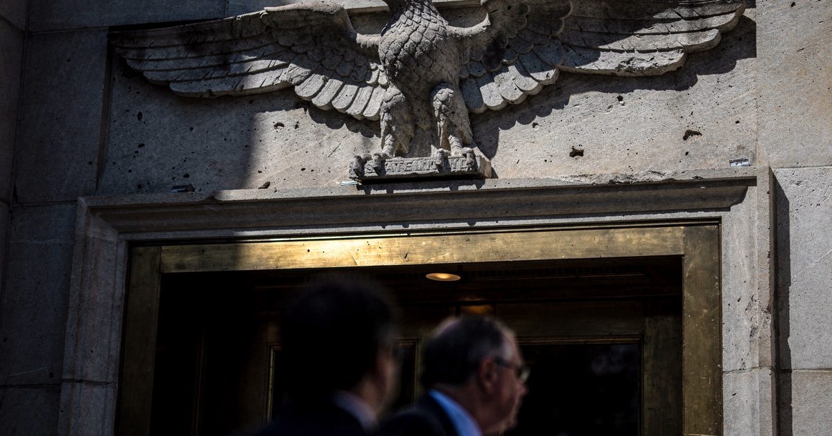 Low-angle close detail of a weathered stone eagle carving above a side entrance to the State Department building in Washington D.C. under stark midday sun, a.