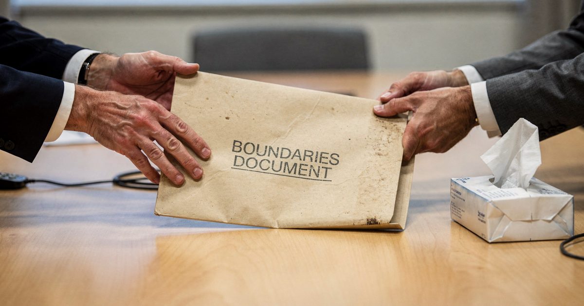 Close detail in flat late-morning light on a veneer meeting table in a Whitehall office, two pairs of hands cropped at the wrists sliding a manila folder.
