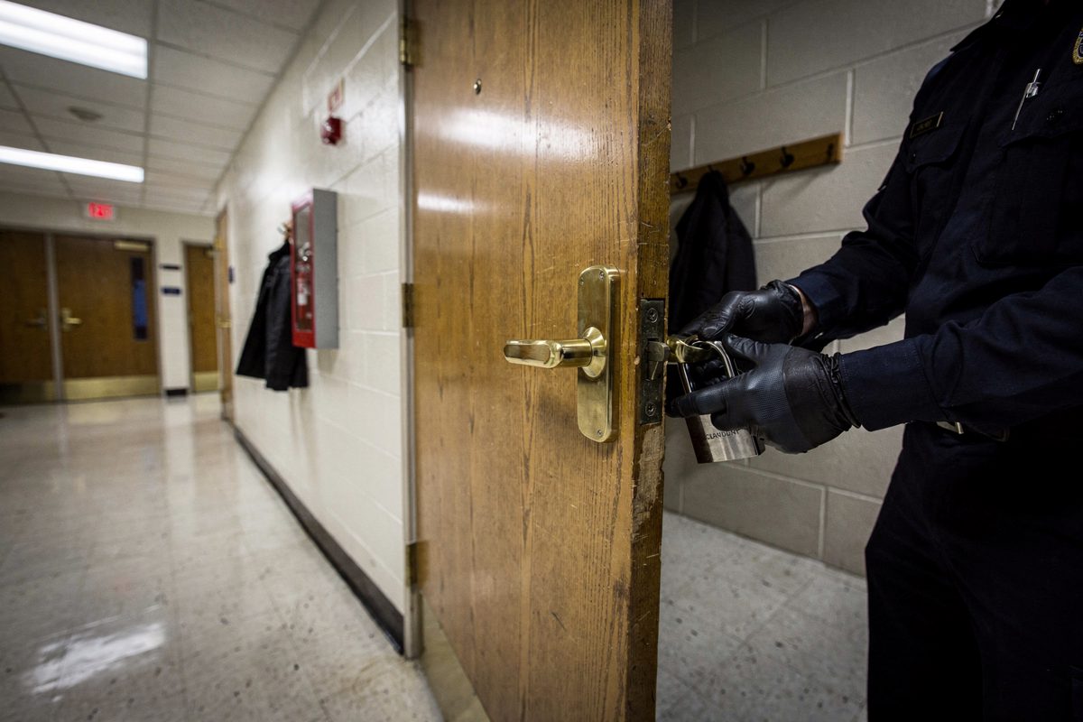 An institutional corridor under flickering overhead lights, where security personnel in dark uniforms are hastily installing a heavy padlock onto the brass.