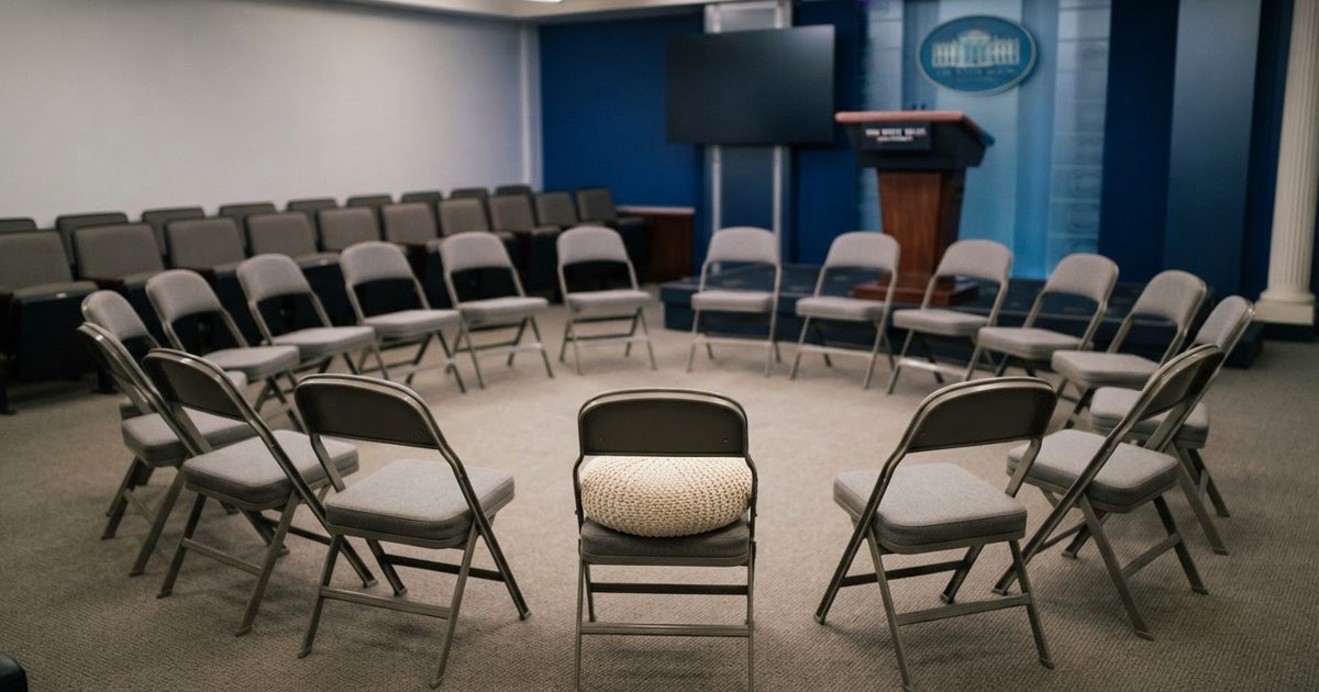 A realistic news photograph of an empty White House-style press briefing room rearranged into a circle of plain chairs, with a soft neutral-colored cushion.