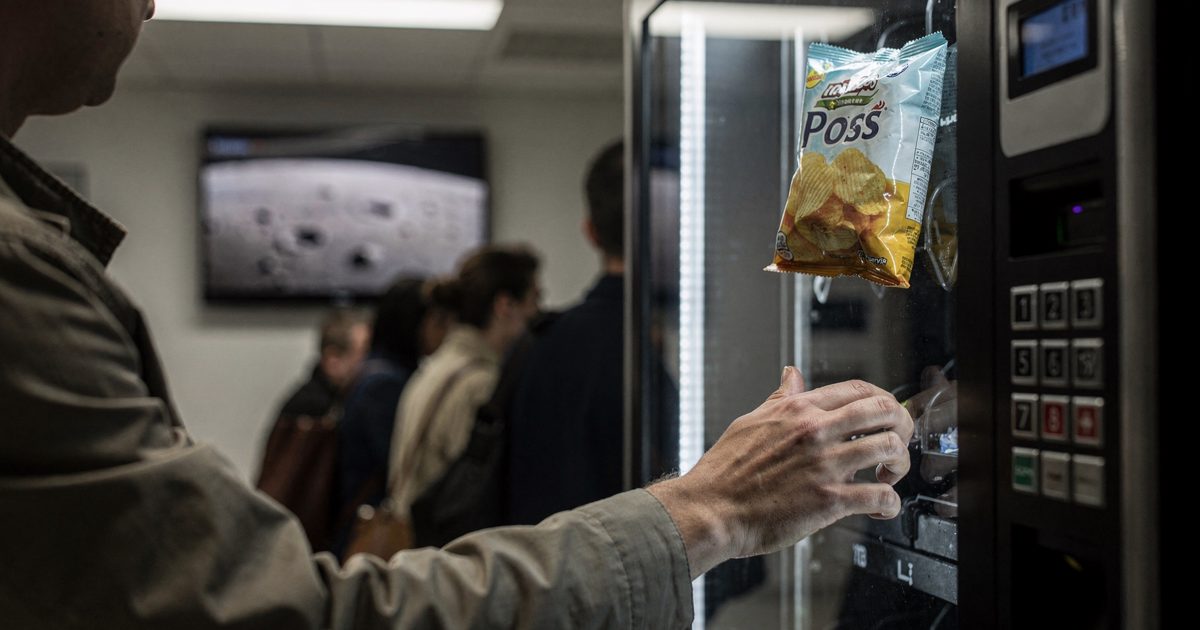 Close-up of a stranger's hands pressing the keypad of a fluorescent-lit corridor vending machine before dawn, a fresh bag of crisps caught mid-fall behind the.