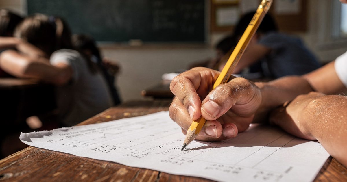 Close detail of a sweating hand gripping a yellow pencil over a blank algebra worksheet, bathed in harsh, blinding afternoon sunlight streaming across a wooden.