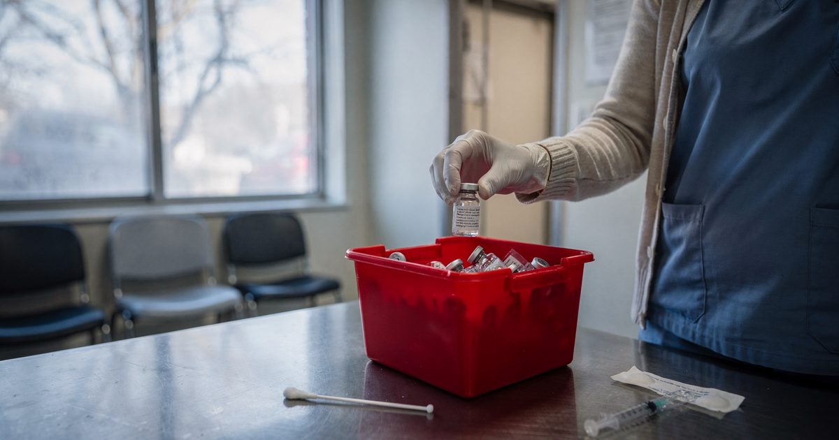 Mid-morning sunlight through a frosted clinic window as a nurse cropped at the shoulder drops a tiny empty glass vial into a red plastic bin, a fresh cotton.