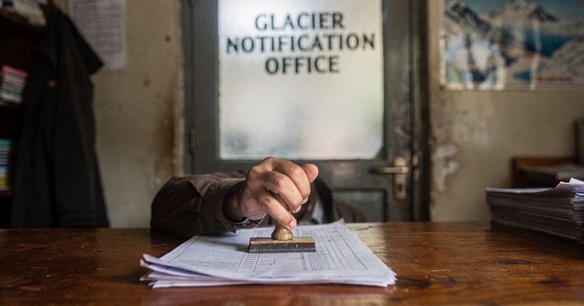 Close midday light on the wooden counter of a small alpine district office as a clerk's hands press a rubber stamp onto a carbon-copy form, a frosted glass.