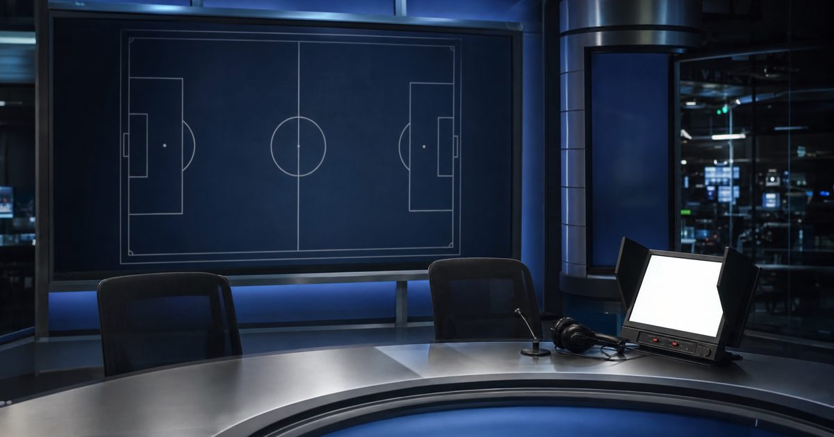 A serious television sports studio with an empty analyst desk, a blank tactical screen and a small review monitor glowing under cool broadcast lights, no.