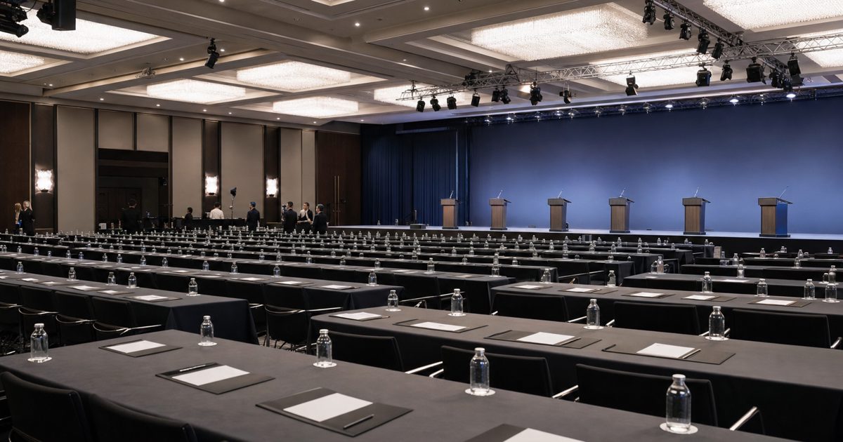 A wide news photograph of an empty international football conference hall prepared for a formal meeting, with lecterns, rows of chairs, document folders and.