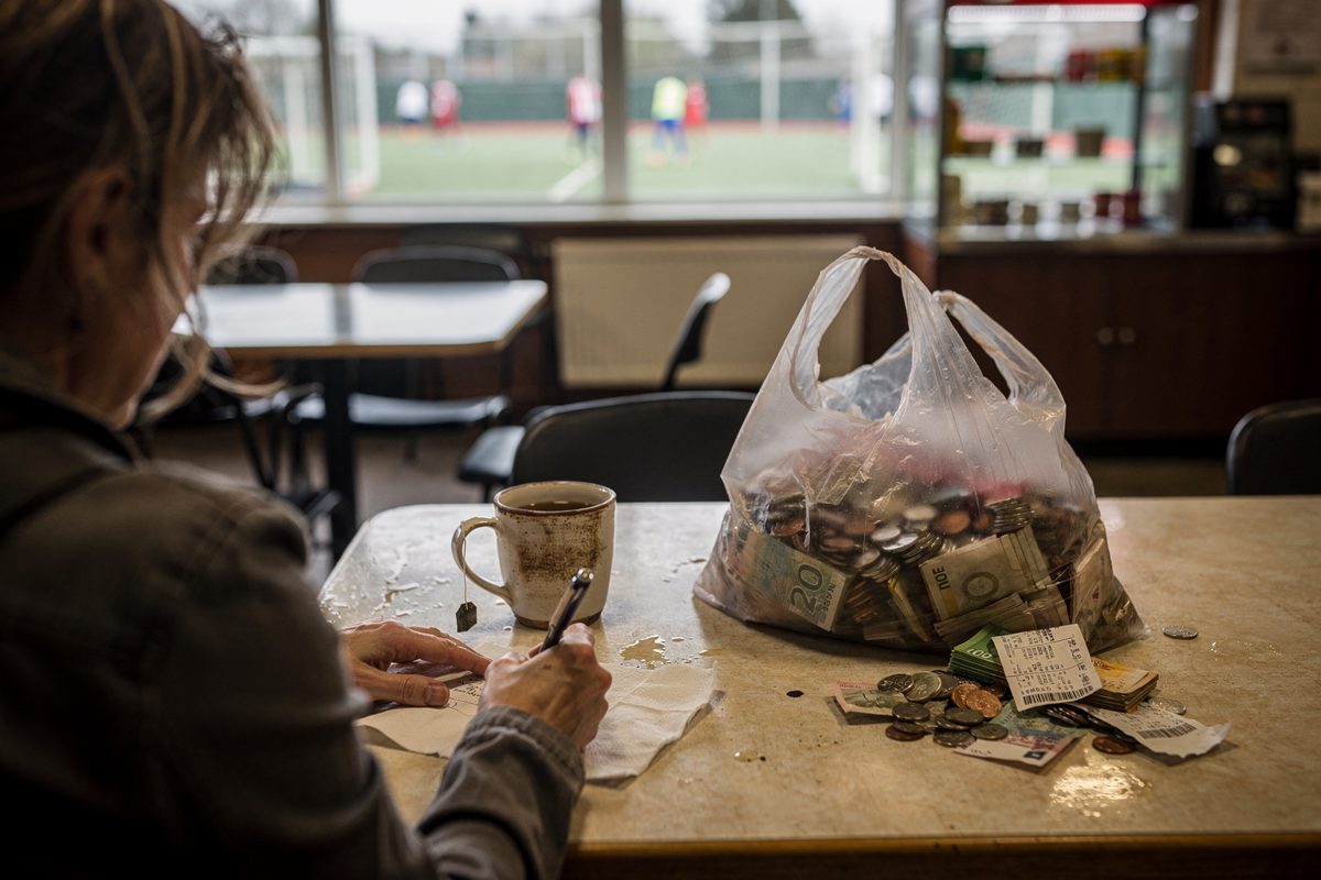 Over-the-shoulder shot at a sticky café table inside a municipal sports centre on a bright Saturday morning, a woman seen only from behind and the shoulder.
