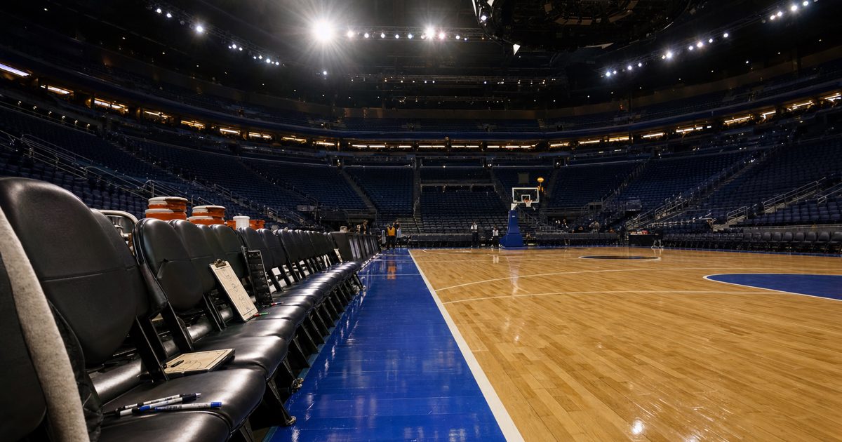 Wide editorial photograph of an empty professional basketball arena before a game, polished court under bright overhead lights, benches prepared, no.