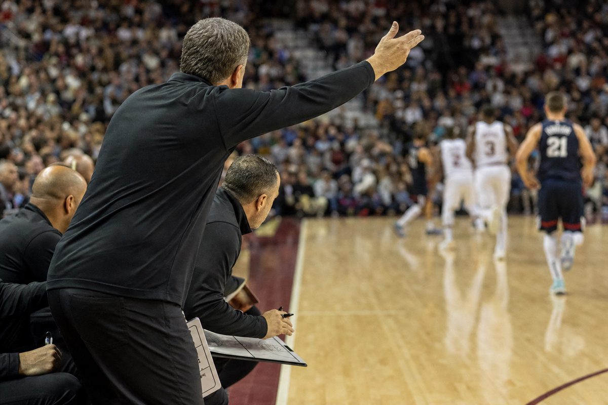 Documentary sports photograph of an anonymous coaching staff gesturing urgently from the sideline during a basketball game, players in generic uniforms moving.