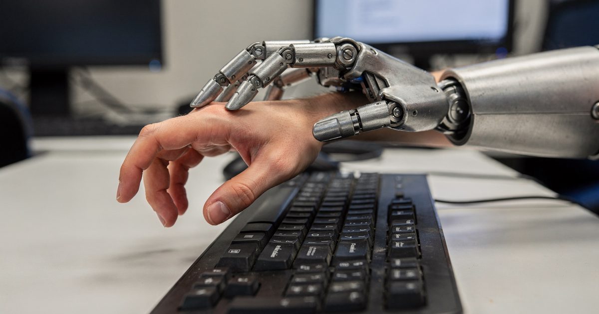A close-up shot under harsh fluorescent office lights showing a pale human hand hovering nervously over a computer keyboard, while a heavy, brushed-steel.