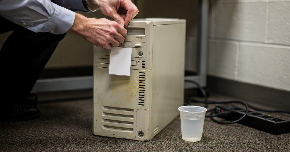 In a windowless state government annex under hard afternoon fluorescent tubes, a staffer's hands clip a blank visitor badge onto the top handle of a beige.