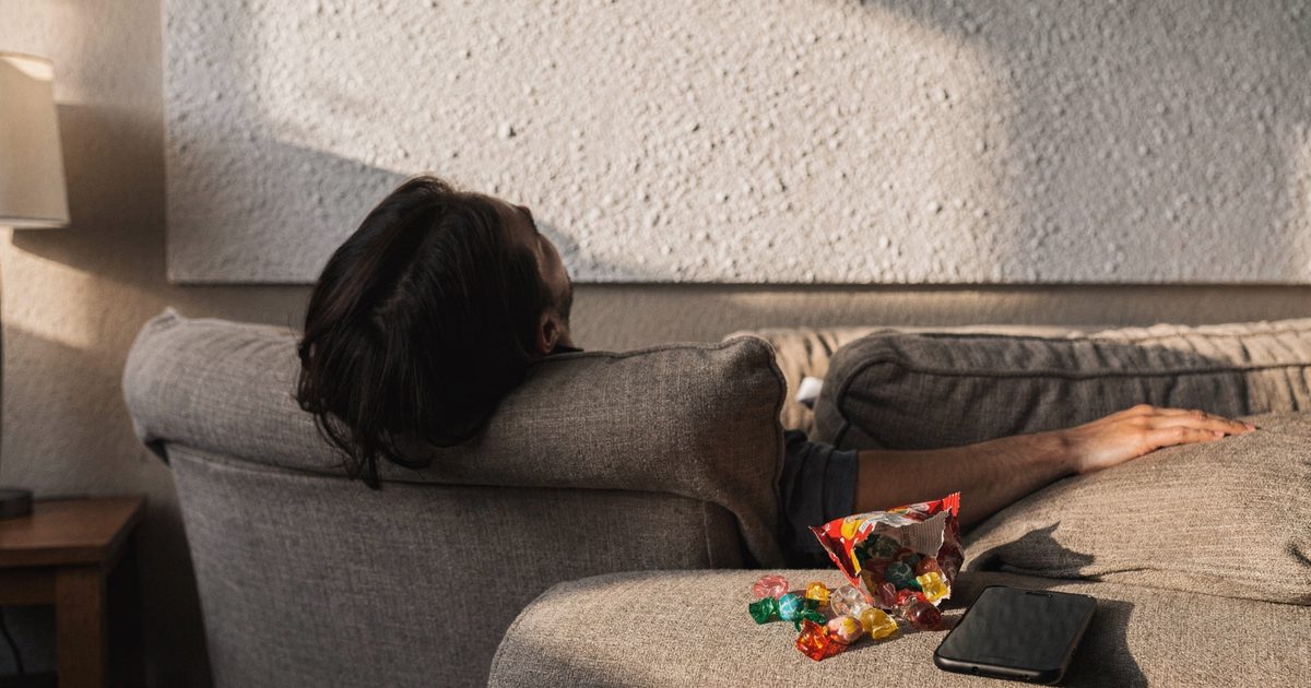 Warm late-afternoon light in a suburban living room, a person reclining on a couch shot from behind with their head tipped toward a blank popcorn ceiling, a.
