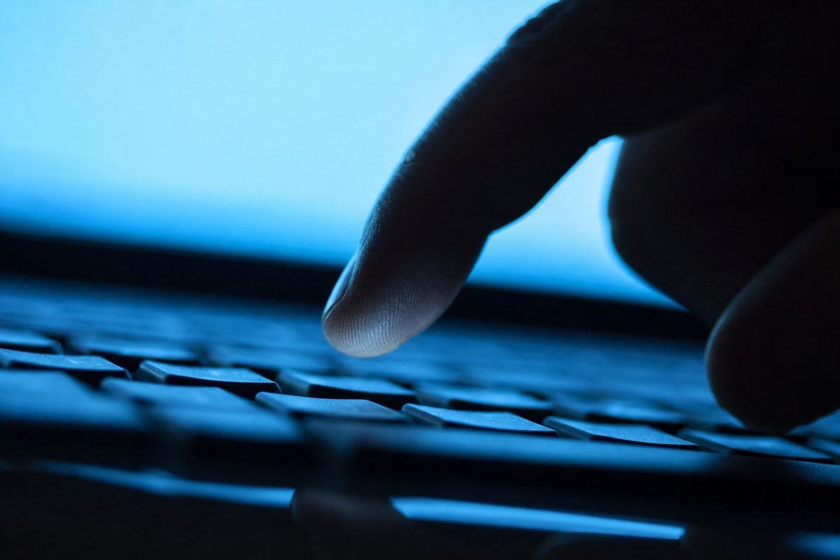 A dramatic, cinematic close-up of a human finger hovering intensely over a generic computer keyboard, illuminated by a harsh blue screen light, as if about to.
