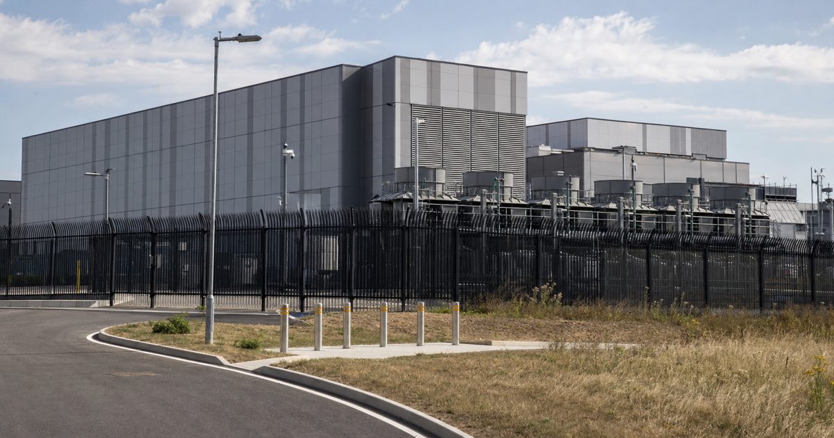 Documentary news photograph of vast metal-clad datacentre buildings on an industrial estate in Slough during a hot summer afternoon, cooling equipment and.