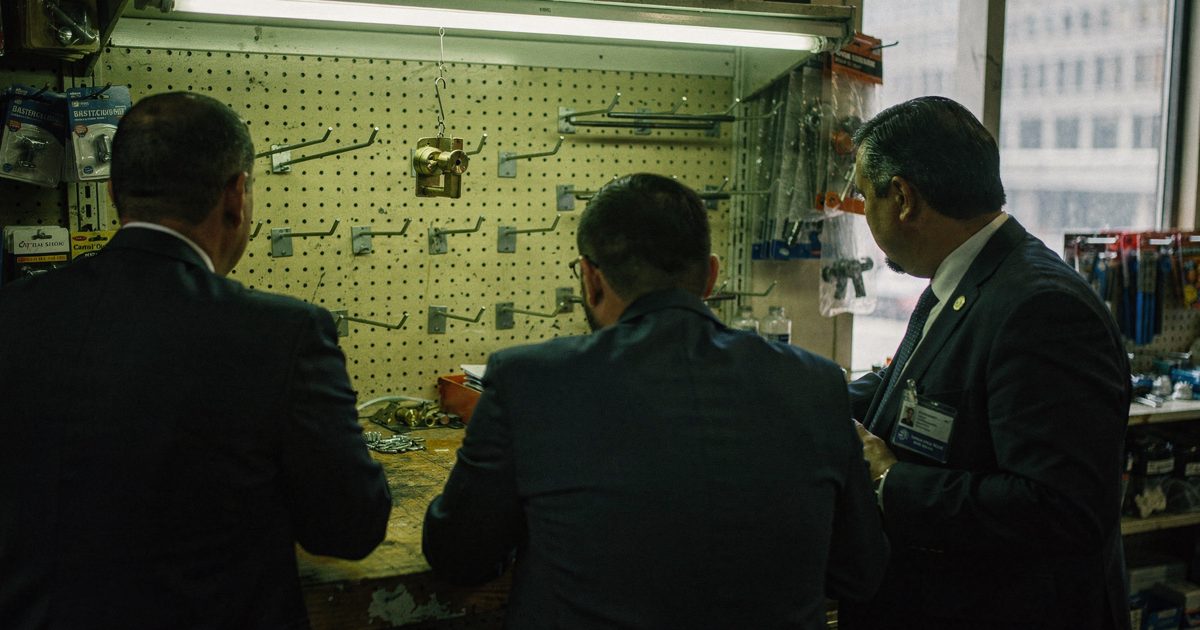 Medium shot under harsh overhead strip light inside a small Capitol Hill hardware shop at lunchtime, three customers in suit jackets and congressional staff.