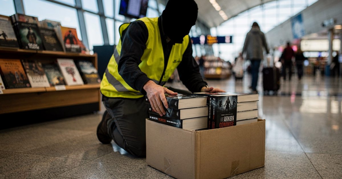 Low-angle shot from the floor of a brightly lit airport terminal concourse on a Sunday morning, a worker wearing a high-visibility vest kneeling to pack thick.