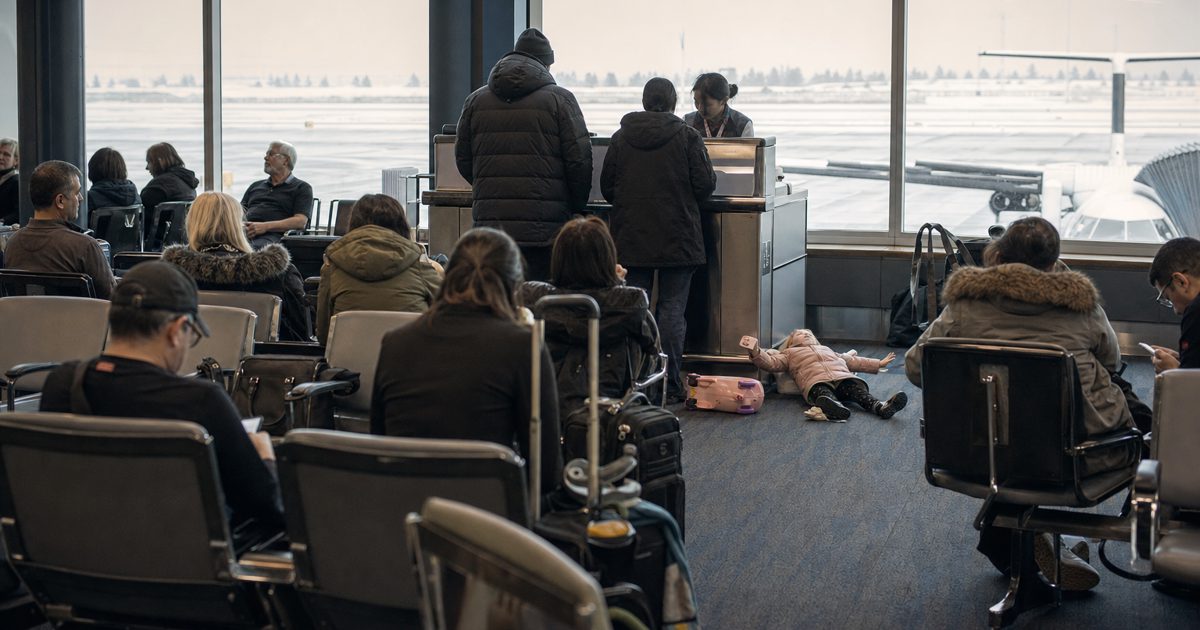 Documentary news photograph inside a Canadian airport departure gate after a cancellation, weary passengers seated with carry-on luggage, airline staff.