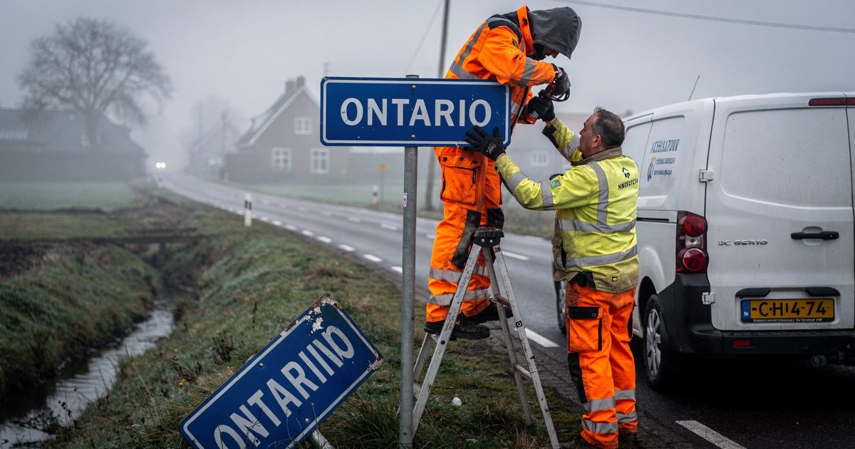 Close shot at a misty village edge in early morning light, two workmen seen from behind on a stepladder unbolting a blue place-name sign, a replacement sign.