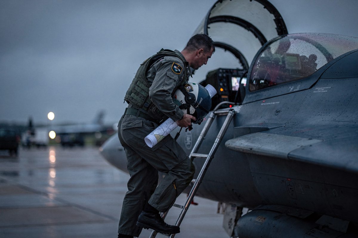 Medium shot at blue hour on a rainy Lincolnshire RAF station flight line, a pilot cropped at the shoulders climbing the ladder into a Typhoon cockpit with a.