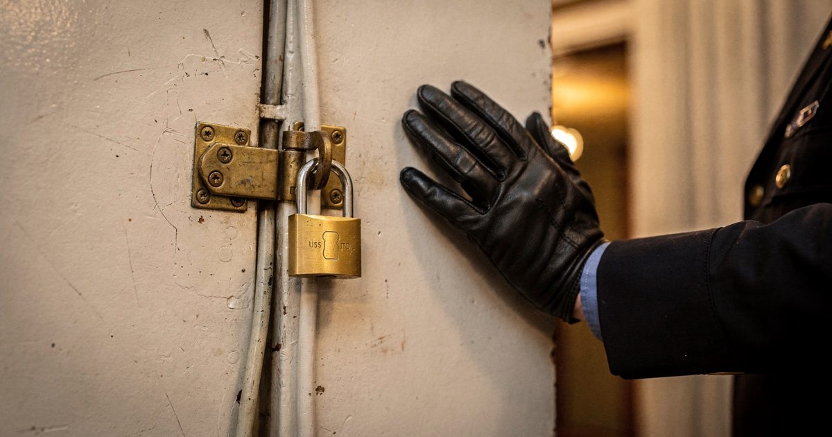 Close detail backstage at Stockholm City Hall under warm tungsten house light, a brass hasp and padlock newly fitted over a wall-mounted theatre lighting fader.