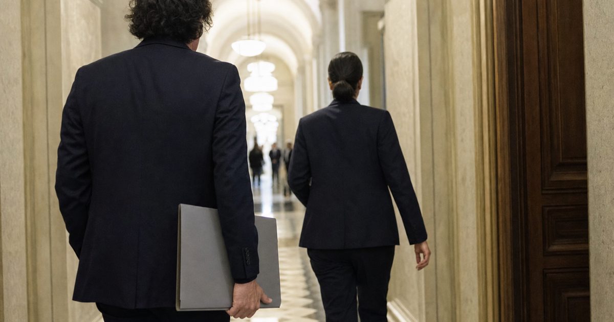 Documentary news photograph of anonymous diplomatic staff carrying a plain grey folder through a formal government corridor, faces turned away, subdued natural.