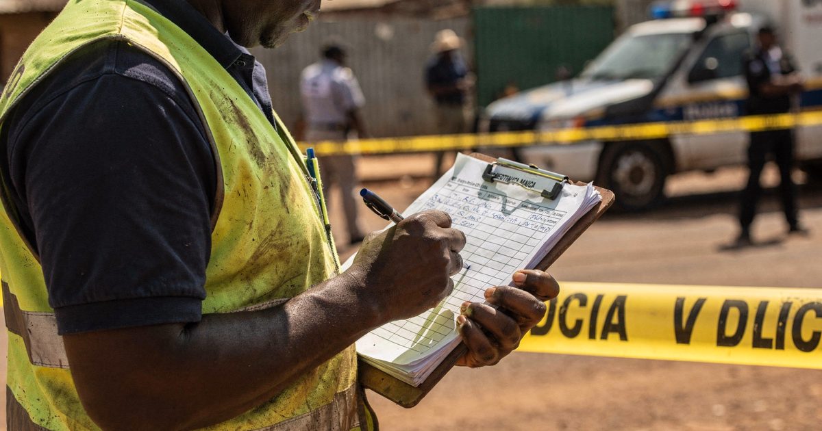 Close shot from chest height of a municipal worker in a faded high-visibility vest standing near a police tape cordon in harsh midday sunlight, marking off.